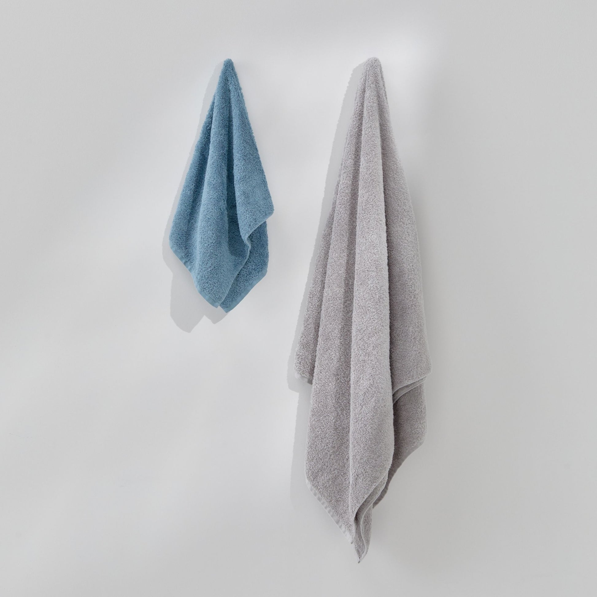 Two towels, one blue and one gray, hanging on a white wall.