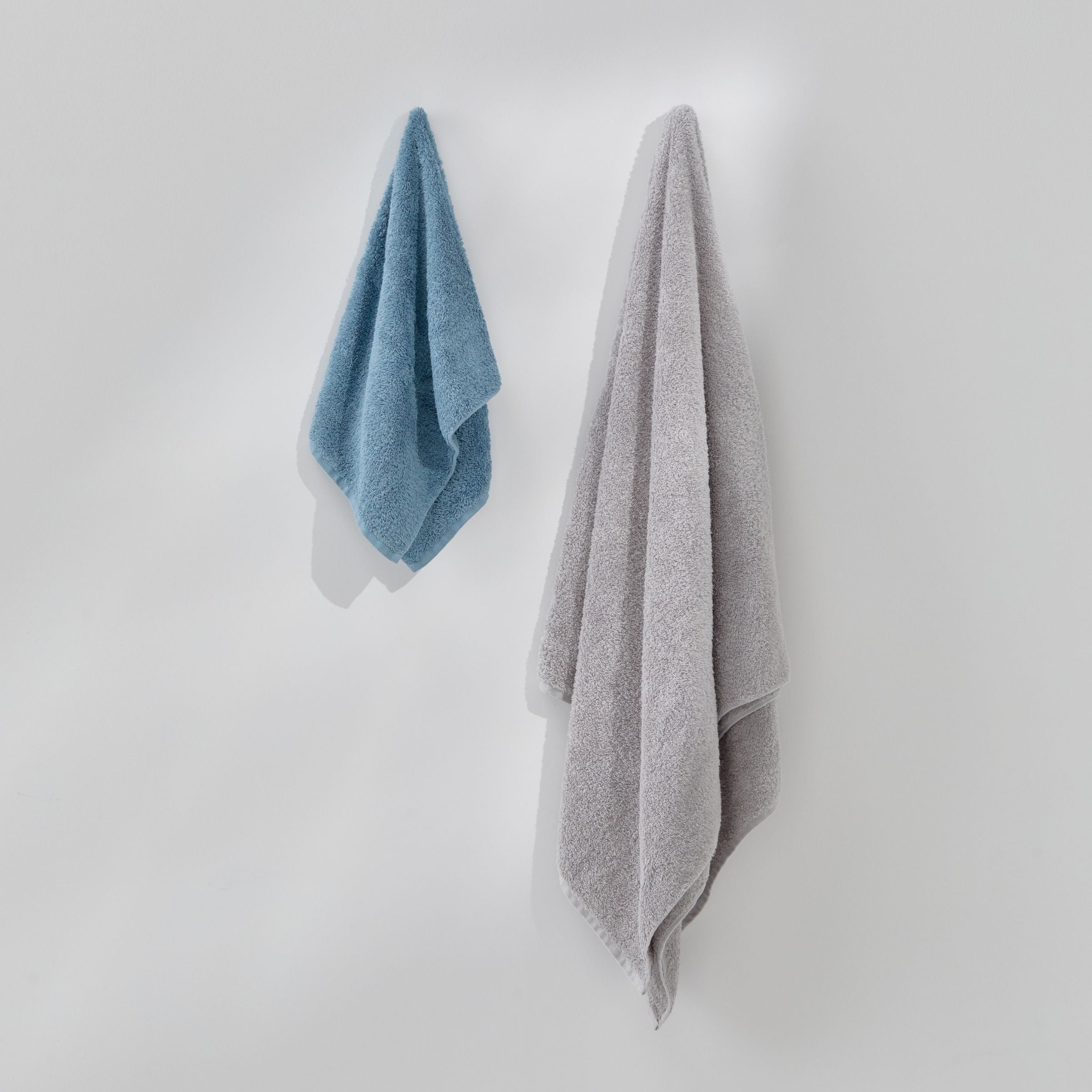 Two towels, one blue and one gray, hanging on a white wall.